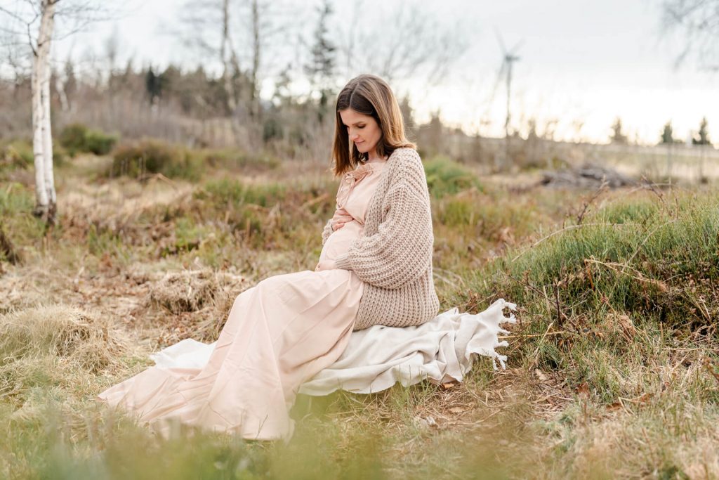 Schwangere sitzt auf einer Decke in schöner Landschaft und streichelt ihren Babybauch