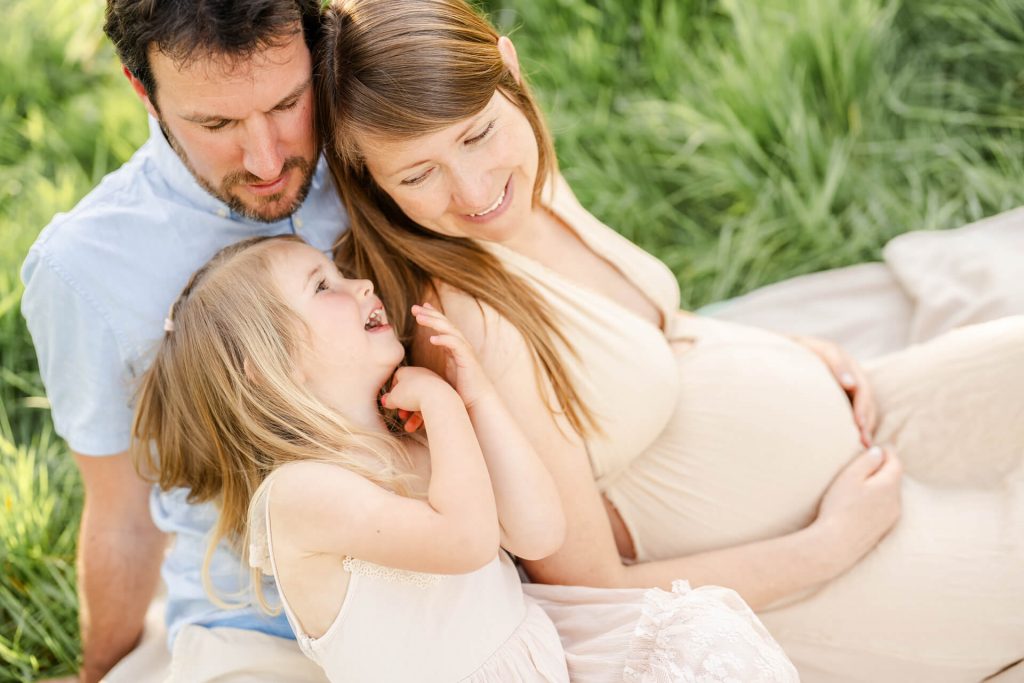 Schwangere Mama, Papa und Tochter kuscheln sich aneinander