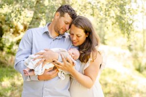 Mama und Papa mit ihrem Baby / Neugeborenen im Arm draußen auf einer Wiese mit Bäumen