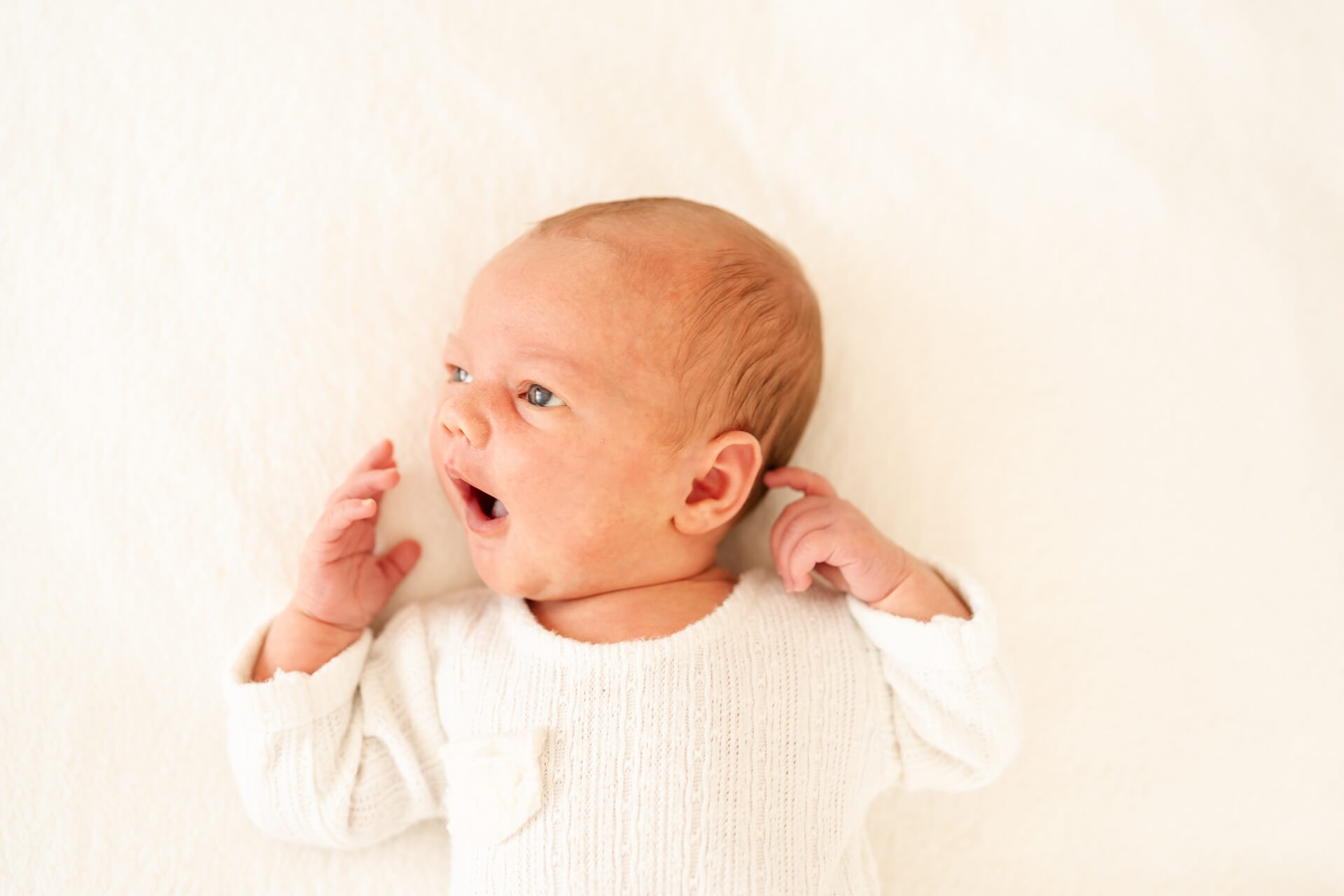 Neugeborenes liegt auf einer Decke und gähnt
