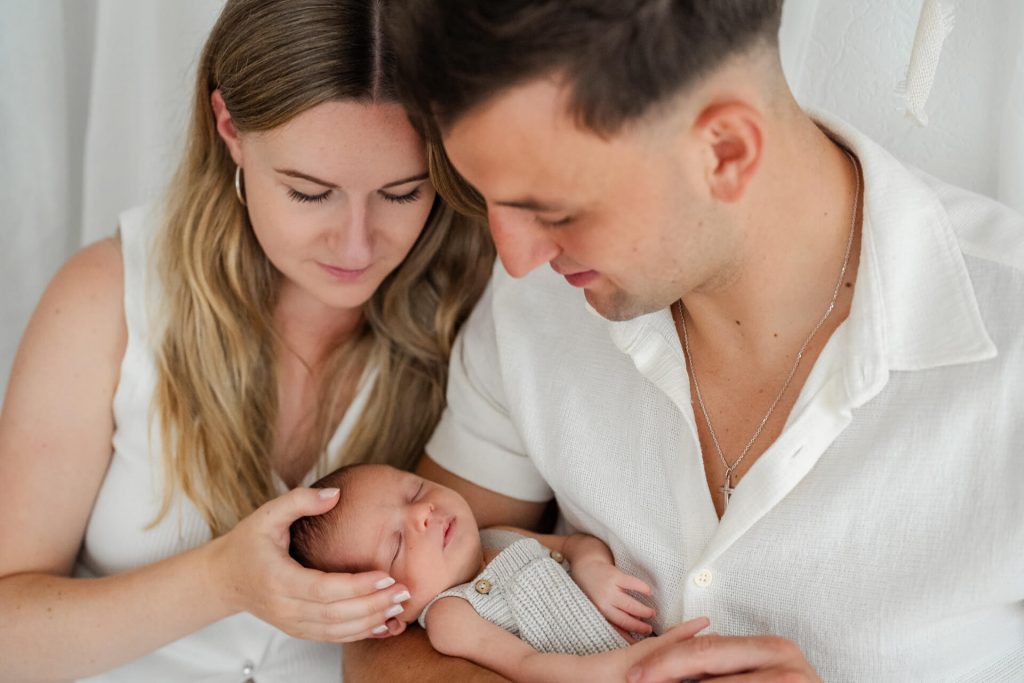 Mama und Papa kuscheln sich aneinander und halten ihr Neugeborenes in den Händen