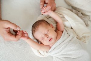 Baby ist eingekuschelt in weiche Decken und wird an den Händen von Papa gehalten