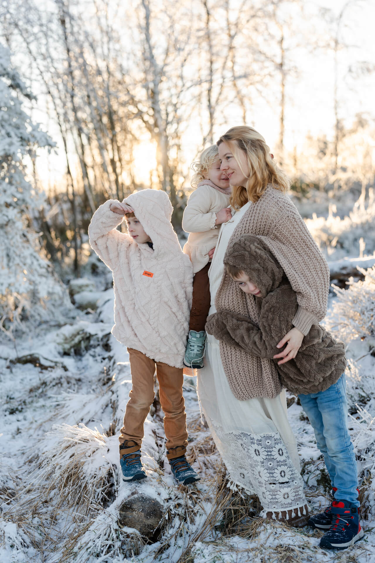 Mama steht mit ihren drei Kindern in Schneelandschaft, im Sonnenuntergang