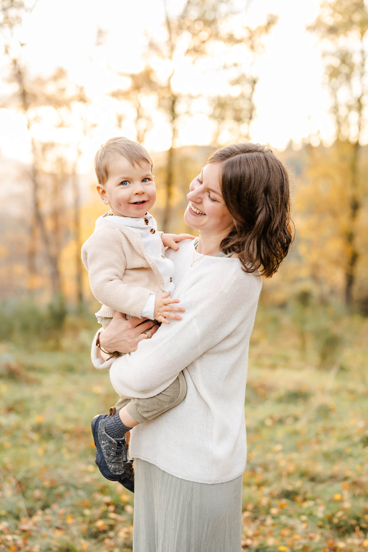 Mama hält ihren kleinen Sohn auf den Armen und lächelt ihn an, er schaut in die Kamera