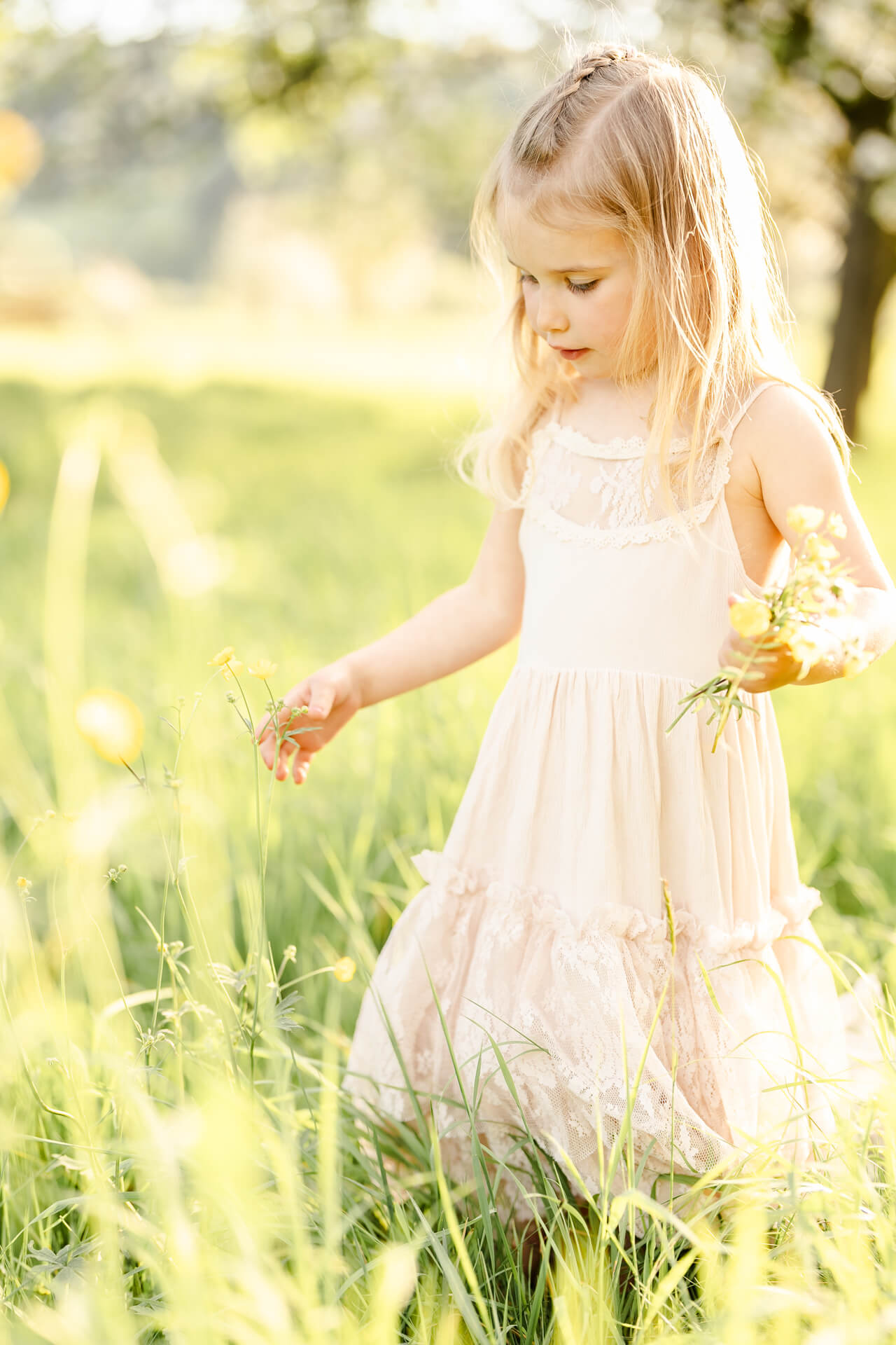 Mädchen mit Spitzenkleid läuft über eine Wiese und sammelt Blümchen für einen Blumenstrauß